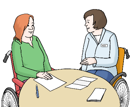 Zwei Personen sind an einem runden Tisch. Beide sitzen im Rollstuhl. Vor ihnen liegen Papiere und ein Stift. Die Frau rechts erklärt etwas und gestikuliert dabei mit ihrer Hand.